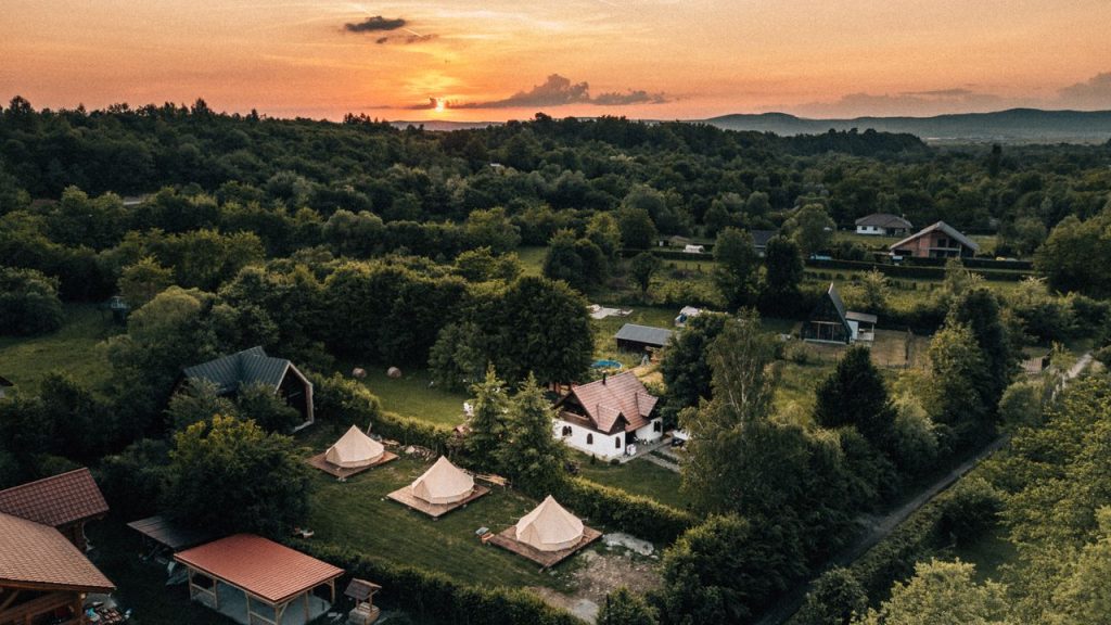 Aerial view of Romania's lush countryside with tents and homes at sunset.